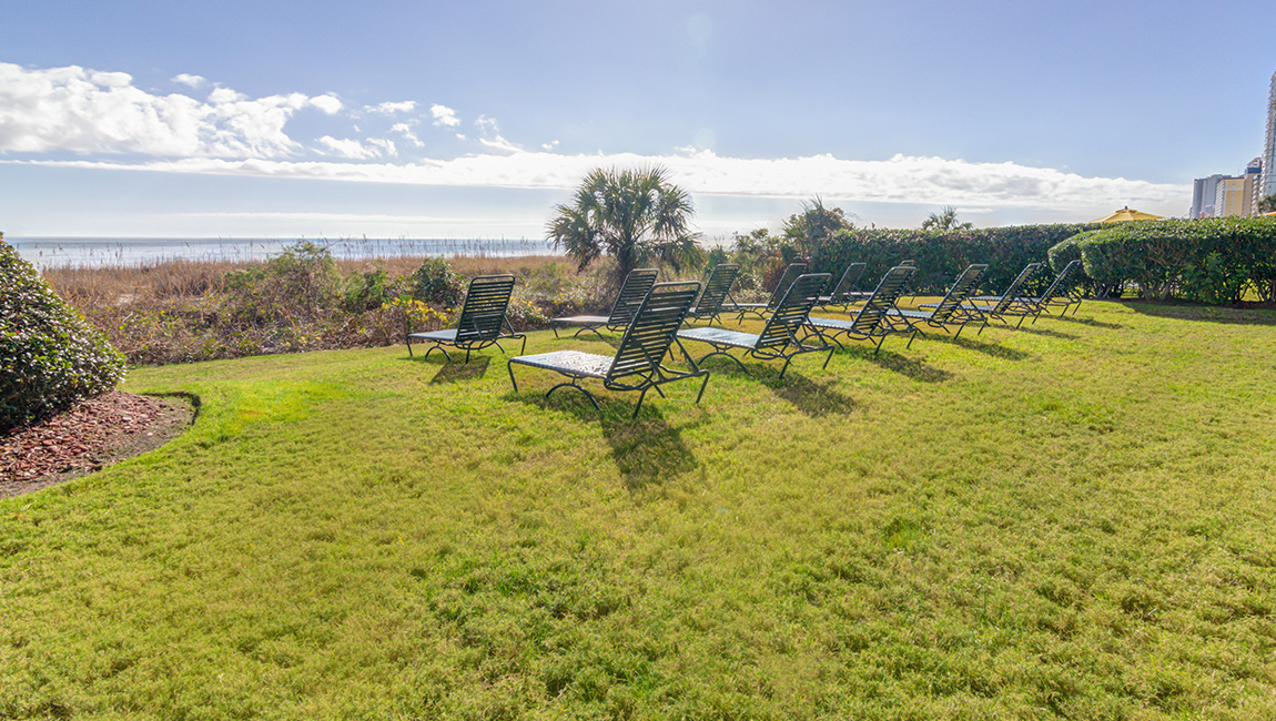 A well-manicured lawn with lounge chairs overlooking the beach.