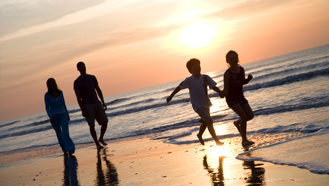 A family of four enjoys a sunset walk on the beach.
